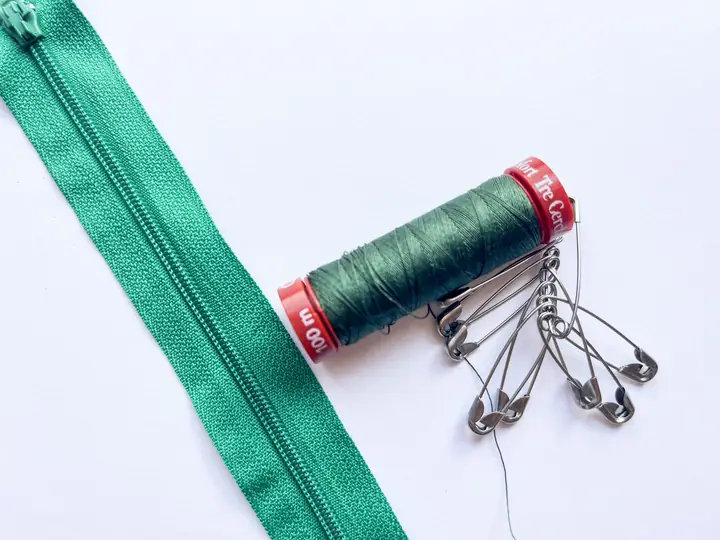 A reel of green thread and safety pins beside a green zip