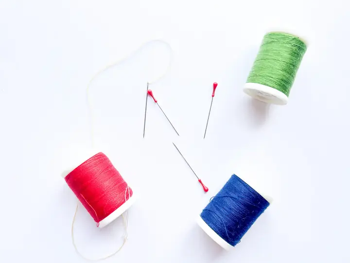 Red, green and blue reels of thread with pins on a white table